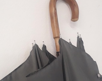Puede incluir: Un paraguas gris oscuro con un mango de madera. El paraguas está cerrado y plegado.