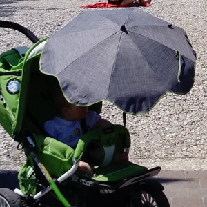 Può includere: Un passeggino verde con un ombrello nero e grigio. Il passeggino ha una maniglia nera e un sedile nero e bianco. Un bambino è seduto nel passeggino.