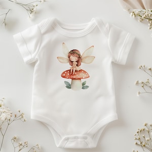 Puede incluir: Un body blanco para beb&eacute; con una ilustraci&oacute;n de acuarela de una hada sentada en un hongo. El hada tiene el pelo casta&ntilde;o, una corona de flores y alas. El hongo es rojo con manchas blancas.