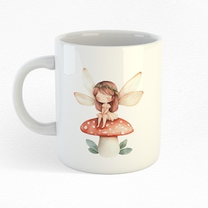Puede incluir: Taza de cer&aacute;mica blanca con una ilustraci&oacute;n de acuarela de un hada sentada en un hongo rojo y blanco. El hada tiene el pelo casta&ntilde;o, un vestido blanco y alas blancas.