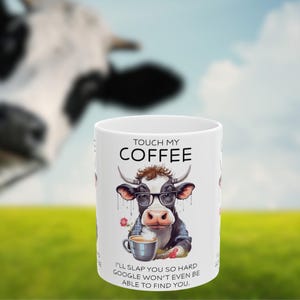 May include: White ceramic coffee mug with a black and white cow wearing glasses and a blue shirt. The mug has the text "Touch My Coffee" and "I'll slap you so hard Google won't even be able to find you."