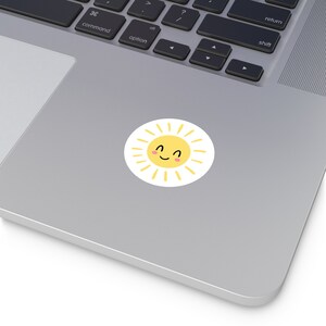 May include: A yellow sun with a smiling face and rosy cheeks. The sun has a white outline and yellow rays.