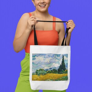 K&ouml;nnte beinhalten: Eine wei&szlig;e Einkaufstasche mit schwarzen Henkeln, die ein Gem&auml;lde einer Landschaft mit einem hohen, schlanken Baum im Vordergrund zeigt. Das Gem&auml;lde ist im Stil von Vincent van Gogh gehalten.