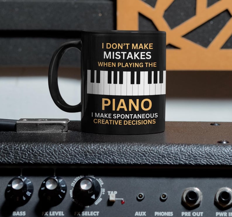 May include: Black coffee mug with a white piano keyboard graphic and the text "I don't make mistakes when playing the piano. I make spontaneous creative decisions."