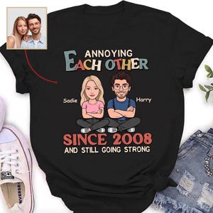 Puede incluir: Camiseta negra con el texto "Annoying Each Other Since 2008 and Still Going Strong". Presenta ilustraciones de dibujos animados de una pareja, Sadie y Harry, con sus nombres debajo. Una peque&ntilde;a foto de la pareja est&aacute; en la esquina superior izquierda.