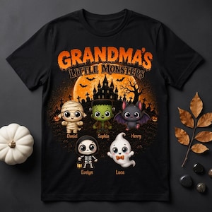 May include: A black t-shirt featuring a graphic print with the text "GRANDMA'S LITTLE MONSTERS" above a Halloween scene. The design includes a mummy, Frankenstein's monster, a bat, a skeleton, and a ghost with the names Daniel, Sophia, Henry, Evelyn, and Luca.