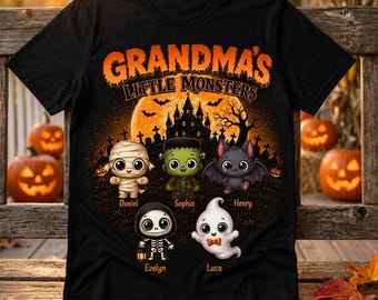Puede incluir: Una camiseta negra con el texto naranja GRANDMA'S LITTLE MONSTERS sobre una escena de Halloween con una casa encantada, una luna llena y cinco personajes de dibujos animados: una momia, Frankenstein, un murciélago, un esqueleto y un fantasma.