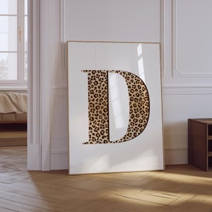May include: A white framed poster with a large letter "D" in a leopard print pattern.