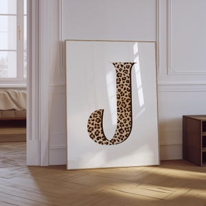 May include: A white framed poster with a large letter J printed in a leopard print pattern.