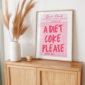 May include: A framed pink print with the words "A Diet Coke Please" in bold, red letters. The print resembles a guest check and includes the words "Guest Check" and "Thank You!"