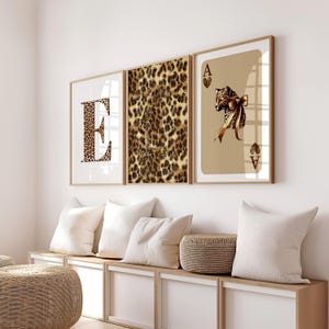 May include: Three framed wall art pieces. The first features the letter "E" in a leopard print pattern. The second is a leopard print design. The third is a playing card with a leopard and bow illustration. All are in wooden frames.