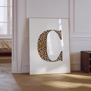 May include: A white framed poster with a large letter "C" printed in a leopard print pattern.