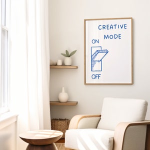 Może przedstawiać: Biały wydruk w ramie z tekstem "CREATIVE MODE" i niebieską ilustracją przełącznika w pozycji "włączony". Wydruk wisi na białej ścianie.