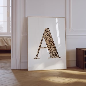 May include: A framed art print featuring the letter "A" in a bold, serif font. The letter is filled with a leopard print pattern in shades of brown and black. The artwork is displayed against a white background.