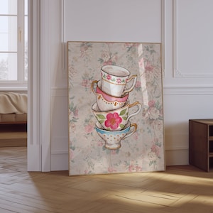 Puede incluir: Una impresión artística enmarcada que presenta una pila de cuatro tazas de té. Las tazas de té están pintadas con acuarela con diseños florales y de lunares. El fondo es un estampado floral en tonos rosas y beige. El marco es de color marrón claro.