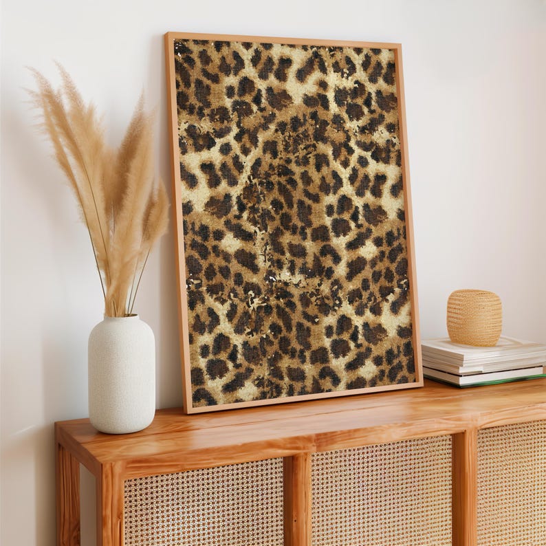May include: A framed print featuring a brown and tan leopard print pattern. The print is hanging on a wall above a wooden console table with a woven rattan front.
