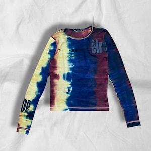 Może przedstawiać: Długi rękaw tie-dye koszula z mieszanką żółtych, niebieskich i bordowych kolorów. Słowo "OP" jest wydrukowane na lewym rękawie, a słowo "être" jest wydrukowane w prawym górnym obszarze klatki piersiowej. Koszula ma okrągły dekolt.