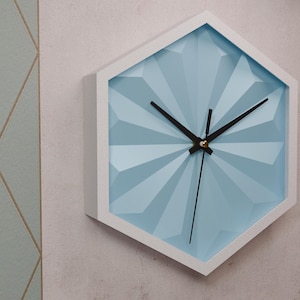 May include: A hexagonal wall clock with a white frame and a light blue face. The clock has black hands and a gold center.