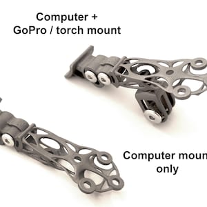 Peut inclure: Deux supports d'ordinateur gris, l'un avec un support GoPro/torche et l'autre pour ordinateur uniquement. Les supports ont une conception ouverte complexe avec de multiples points de connexion et des fixations argentées. Le texte sur l'image indique "Computer + GoPro / torch mount" et "Computer mount only."