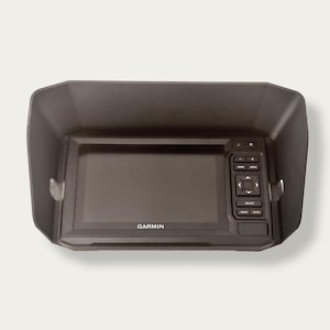 Peut inclure: Un appareil de navigation GPS Garmin noir doté d'un écran rectangulaire et d'un panneau de commande latéral avec des boutons physiques. L'unité est encastrée dans une visière pare-soleil en plastique noir mat pour réduire les reflets.