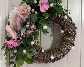 May include: A wicker wreath decorated with pink and white flowers, greenery, and white faux pearl accents.