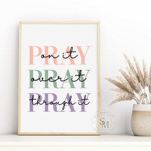 May include: A framed print with the text "Pray on it, Pray over it, Pray through it" in pink, green, and purple lettering. The print is on a white background and has a gold frame.