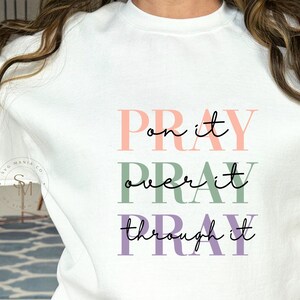 May include: White sweatshirt with the text "Pray on it, Pray over it, Pray through it" in pink, green, and purple lettering.