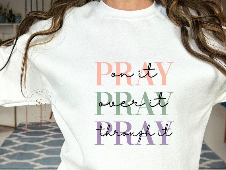 May include: White sweatshirt with the text "Pray on it, Pray over it, Pray through it" in pink, green, and purple lettering.