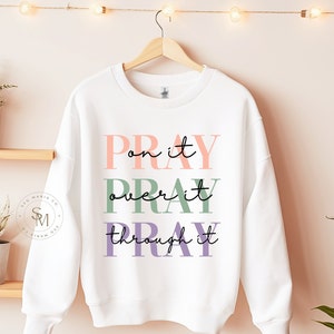May include: White sweatshirt with the text "PRAY on it PRAY over it PRAY through it" in pink, green, and purple lettering.