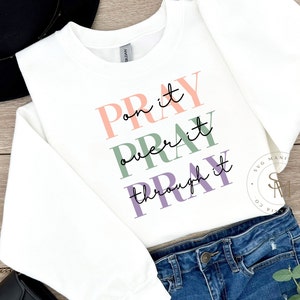 May include: White sweatshirt with the text "Pray on it, Pray over it, Pray through it" in pink, green, and purple lettering.