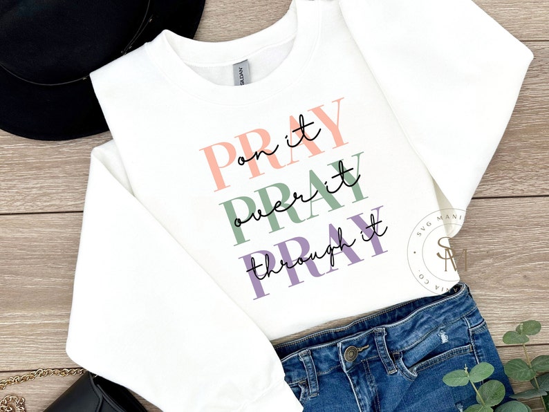 May include: White sweatshirt with the text "Pray on it, Pray over it, Pray through it" in pink, green, and purple lettering.