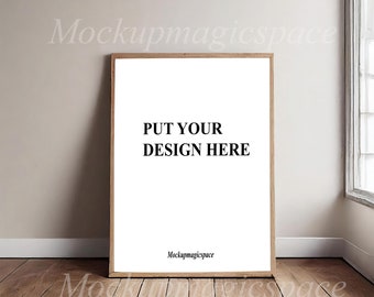 May include: A vertical rectangular poster frame with a light wood finish containing a white display area. The text PUT YOUR DESIGN HERE is printed in black in the center, with the small text Mockupmagicspace at the bottom.