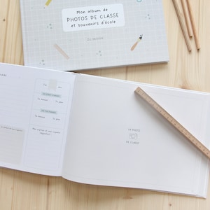 Puede incluir: Un &aacute;lbum de fotos blanco con una portada azul y blanca con el texto "Mon album de PHOTOS DE CLASSE et souvenirs d'&eacute;cole" y el texto "Z&Uuml; DESIGN". El &aacute;lbum est&aacute; abierto en una p&aacute;gina en blanco con un peque&ntilde;o icono de c&aacute;mara y el texto "LA PHOTO DE CLASSE".