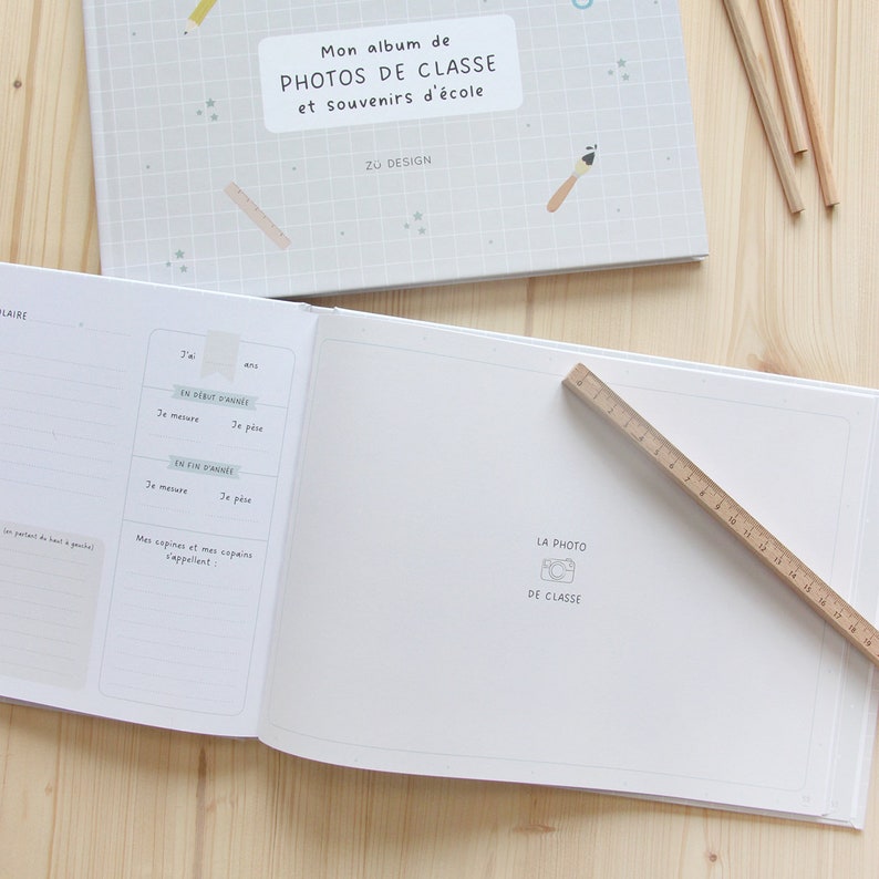 Puede incluir: Un &aacute;lbum de fotos blanco con una portada azul y blanca con el texto "Mon album de PHOTOS DE CLASSE et souvenirs d'&eacute;cole" y el texto "Z&Uuml; DESIGN". El &aacute;lbum est&aacute; abierto en una p&aacute;gina en blanco con un peque&ntilde;o icono de c&aacute;mara y el texto "LA PHOTO DE CLASSE".