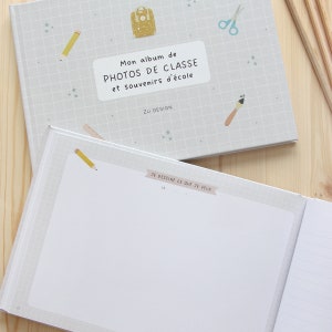 Puede incluir: Un &aacute;lbum de fotos gris y blanco con una mochila azul y amarilla, un l&aacute;piz, una regla, unas tijeras y un pincel en la portada. El texto en la portada dice "Mon album de PHOTOS DE CLASSE et souvenirs d'&eacute;cole Z&Uuml; DESIGN". El interior del &aacute;lbum tiene una p&aacute;gina en blanco con el texto "JE DESSINE CE QUE JE VEUX LE" en la parte superior.