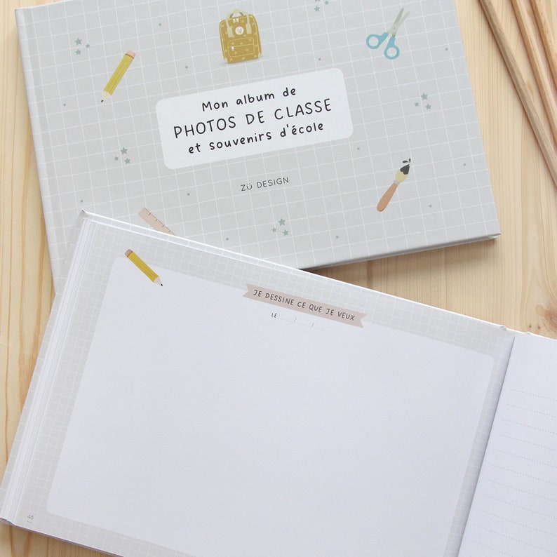 Puede incluir: Un &aacute;lbum de fotos gris y blanco con una mochila azul y amarilla, un l&aacute;piz, una regla, unas tijeras y un pincel en la portada. El texto en la portada dice "Mon album de PHOTOS DE CLASSE et souvenirs d'&eacute;cole Z&Uuml; DESIGN". El interior del &aacute;lbum tiene una p&aacute;gina en blanco con el texto "JE DESSINE CE QUE JE VEUX LE" en la parte superior.