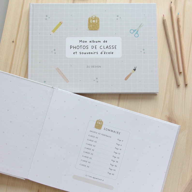 Puede incluir: Un &aacute;lbum de fotos blanco con un patr&oacute;n de cuadr&iacute;cula azul y blanco en la portada. La portada presenta una ilustraci&oacute;n de dibujos animados de una mochila amarilla y el texto "Mon album de PHOTOS DE CLASSE et souvenirs d'&eacute;cole Z&Uuml; DESIGN". El interior del &aacute;lbum muestra una tabla de contenido con los n&uacute;meros de p&aacute;gina para cada secci&oacute;n.