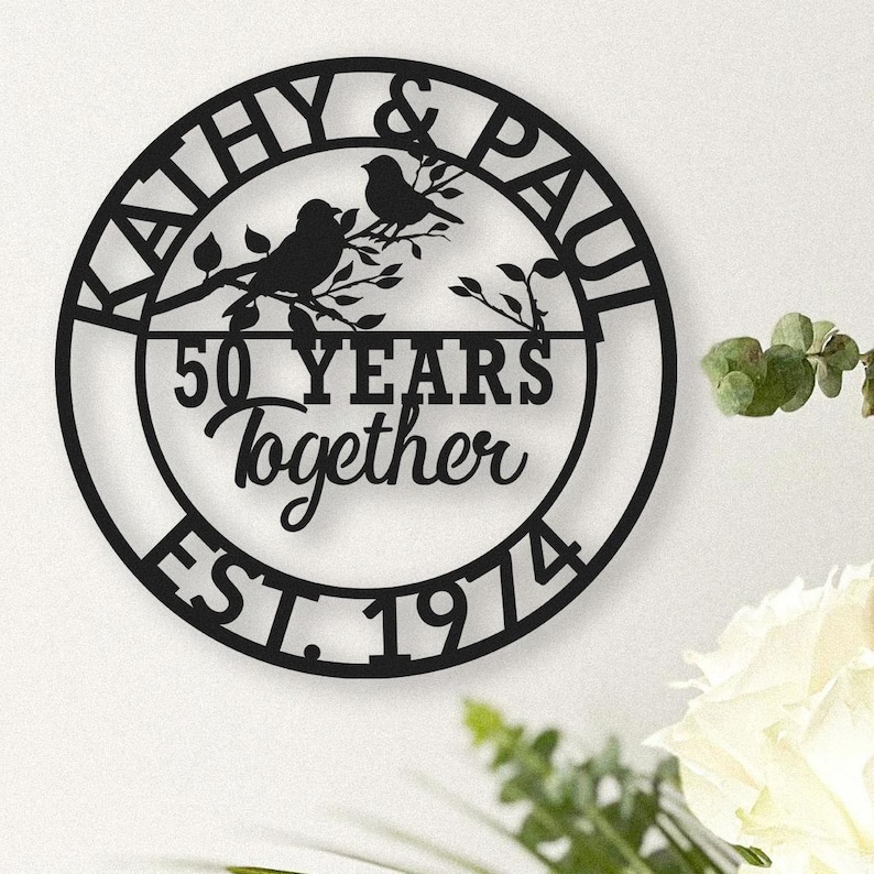May include: Black metal wall art with the names "Kathy & Paul" and the words "50 Years Together EST. 1974". The design includes two birds perched on a branch within a circular frame.
