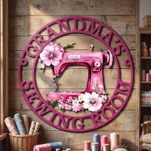 May include: A circular magenta wall sign featuring the text "GRANDMA'S SEWING ROOM" in a bold font. The centre displays a detailed illustration of a pink sewing machine adorned with clusters of light pink and white flowers.