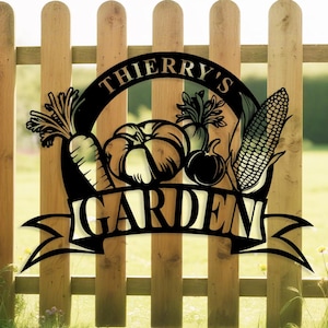 Peut inclure: Panneau de jardin en métal noir avec le texte "THIERRY'S GARDEN" et des illustrations de légumes, dont une carotte, une citrouille, une betterave et du maïs. Le panneau est monté sur une clôture en bois.