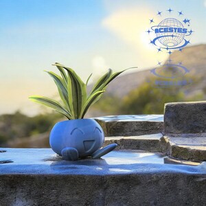 May include: A blue, smiling, spherical planter with a small plant featuring green and yellow striped leaves. The planter has a small arm extending from its side. The background shows a sunny sky and a logo with the text "ACESTES".