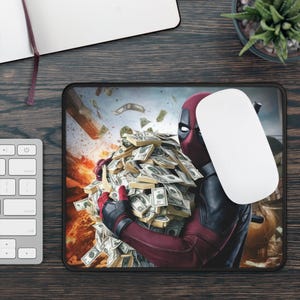 May include: Rectangular mousepad featuring Deadpool holding a large pile of money. The image shows Deadpool in his red and black costume, with a white computer mouse resting on the pad. The background shows money falling from the sky.