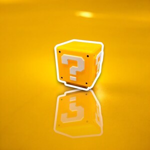 May include: A yellow cube with a white outline and a large white question mark on the front. The cube has a reflective surface, and the background is a matching yellow.