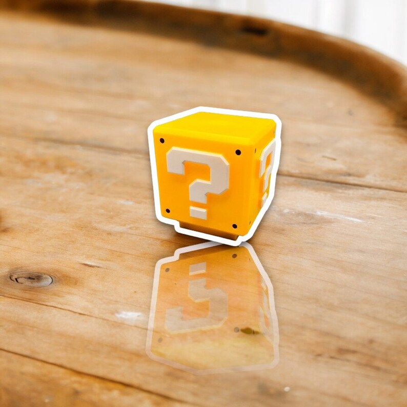 May include: A yellow cube with a white question mark on the front and sides. The cube has a white outline and is sitting on a wooden surface. The cube's reflection is visible on the surface.