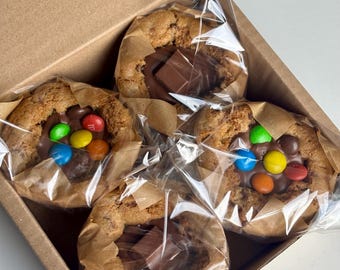 May include: Four cookie cups in a cardboard box. Two cookie cups are topped with colorful M&M's candies and chocolate. The other two cookie cups are topped with a chocolate bar.