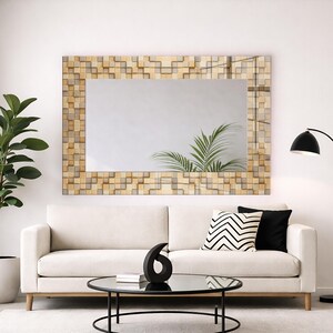 May include: A modern living room featuring a cream-colored sofa, a round glass coffee table, and a large rectangular mirror with a mosaic-style wooden frame. A black floor lamp and a potted plant add to the decor.