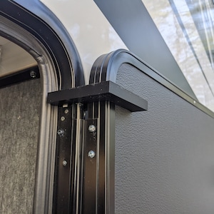 May include: Close-up of a black RV door with a textured surface and a black handle. The door is closed and has a black frame.