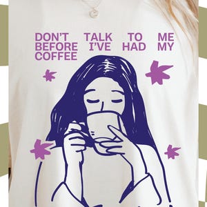 May include: Cream-coloured t-shirt featuring a purple illustration of a person drinking coffee, with the text "DON'T TALK TO ME BEFORE I'VE HAD MY COFFEE" and "BONJOUR!". Includes a "PNG FILE" label.