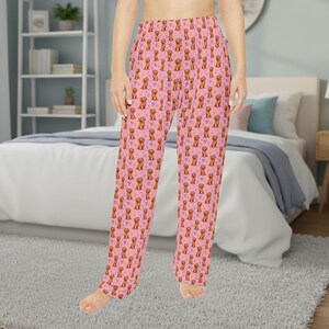 May include: Pink pajama pants with a repeating pattern of brown dogs and purple flowers. The pants are made of a soft material and have a relaxed fit. The pajama pants are suitable for lounging or sleeping.