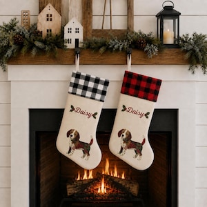 May include: Two off-white Christmas stockings featuring a beagle illustration, holly sprigs, and the name Daisy embroidered in red. One stocking has a black and white buffalo check cuff, while the other has a red and black buffalo check cuff.